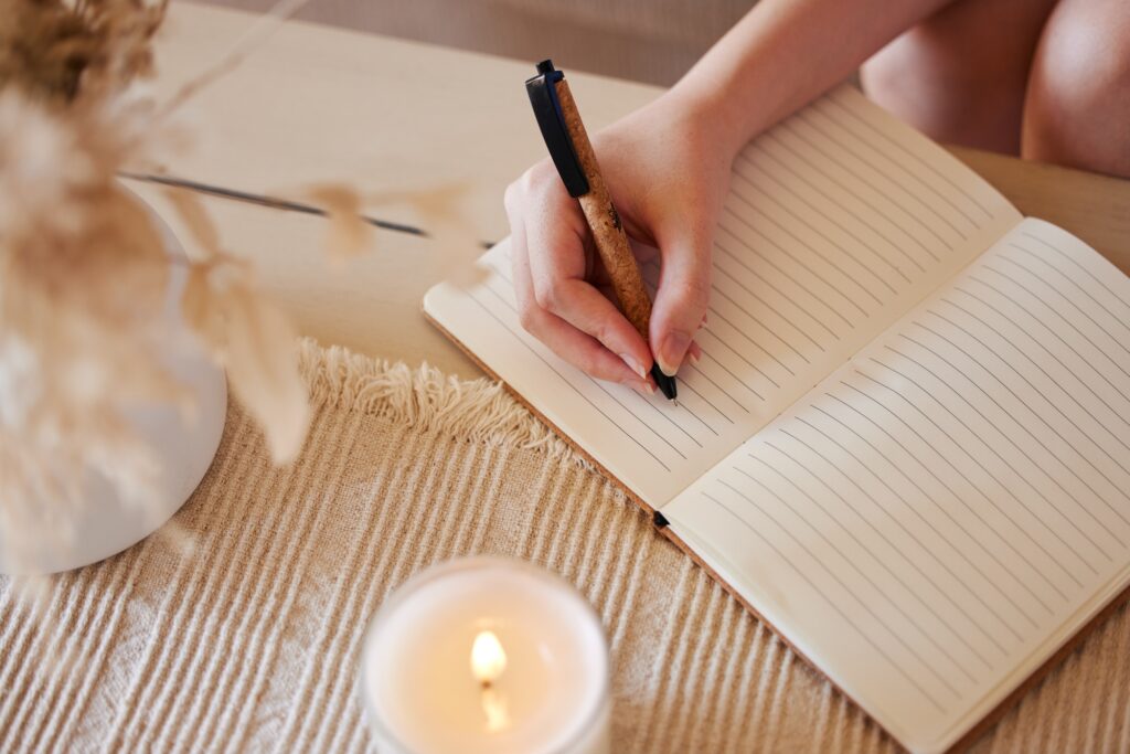 Hand, candle and woman writing in journal in home with top view for calm, peace and relax morning r